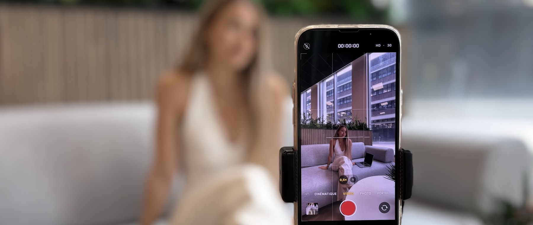 Een creator neemt thuis op de bank een video op met haar telefoon op een statief